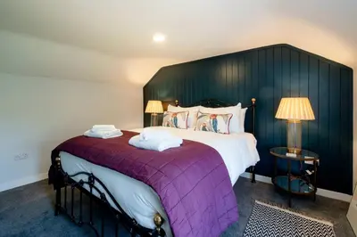 a bedroom with a large bed with a purple blanket at Rose Cottage, Blaxhall - Near Snape Maltings, Orford, Thorpeness & Aldeburgh - Aldeburgh Coastal Cottages in Blaxhall