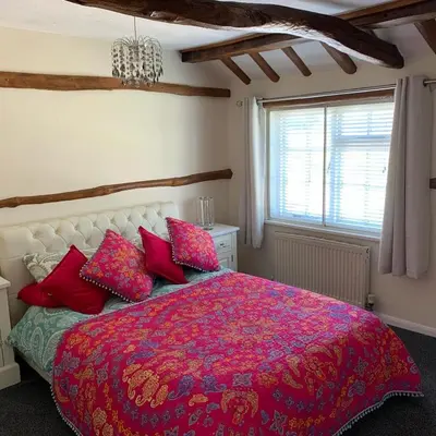 a bedroom with a bed with a red blanket and pillows at Rosemary cottage in Mountnessing