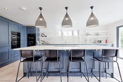 a kitchen with blue cabinets and a large island with bar stools at Mayrose House - 6BR 4BATH Luxe Spacious Retreat in Takeley