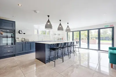 a kitchen with blue cabinets and a bar with stools at Mayrose House - 6BR 4BATH Luxe Spacious Retreat in Takeley