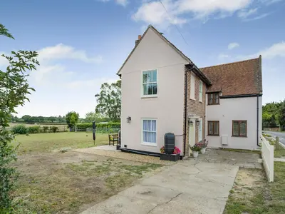 a white house with a field in the background at Oak Tree Cottage in Kirby Cross