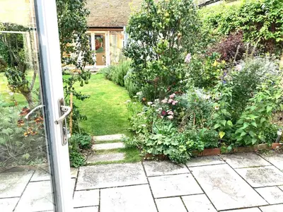 an open door to a garden with flowers and plants at Little Barn in Royston