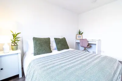 a white bedroom with a large bed with green pillows at Large 6-BDR House in Cambridge in Barnwell Junction Station