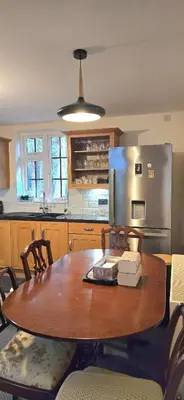 a kitchen with a wooden table and a stainless steel refrigerator at Charming Coach House Cottage in Brentwood in Kelvedon Hatch