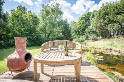 a wooden bench and a vase sitting next to a pond at The Cabin, Ufford in Ufford