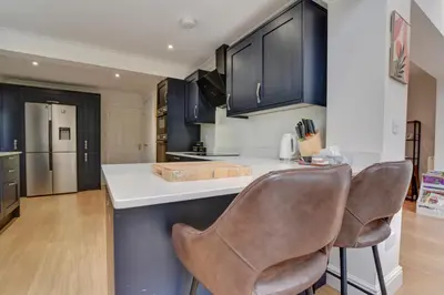 a kitchen with blue cabinets and two bar chairs at Spacious 4 bedroom house in Bishop's Stortford in Thorley