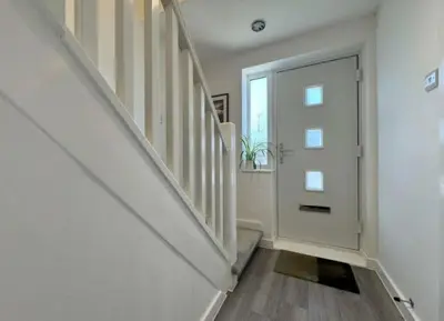 a white hallway with a door and a staircase at The Larks Spacious 3BR Essex in Vange