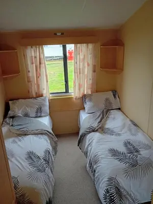 two beds in a small room with a window at Comfortable and Spacious Mobile home - Sleeps 6, in Clacton-on-Sea