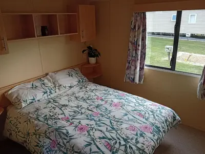 a bedroom with a bed with a floral comforter and a window at Comfortable and Spacious Mobile home - Sleeps 6, in Clacton-on-Sea