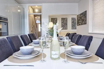 a table with chairs and a bottle of wine and glasses at The Opulent Property Project Southend Beach House Sleeps 8 Free Parking x 2 Perfect for Contractors 4 King Beds or 8 Single Beds in Southend-on-Sea