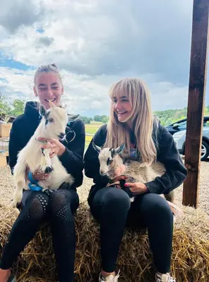 two women are sitting on hay holding goats at Goldings detached Barn farm stay in Hertford