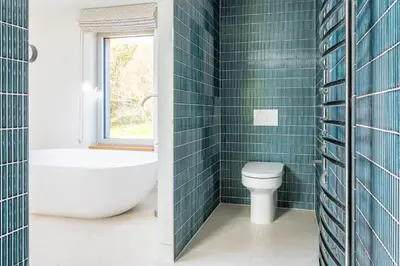 a bathroom with blue tiled walls and a toilet and a window at Heath House 8 in Thorpeness