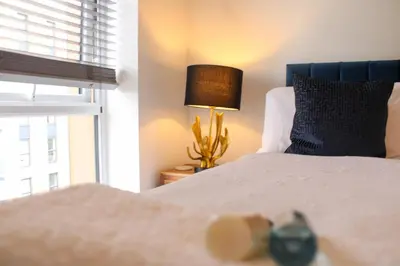 a bedroom with a bed with a lamp and a window at Stylish Essex Apartment, Balcony & Scenic Views in Harlow