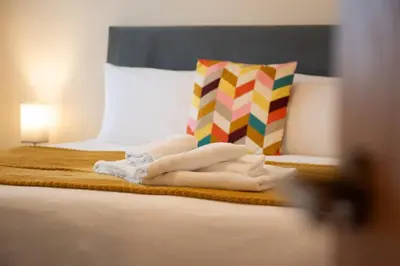 a bed with towels on it with a colorful pillow at 1 The Royal Serviced Apartments, Harwich SuperKing Bed, Parking, Fast WiFi in Parkeston