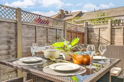 a table with plates and wine glasses on a balcony at Riverside Cottage Retreat Hertford Town Sleeps 6 in Hertford