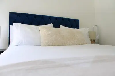a white bed with white pillows and a blue headboard at The Ivy Abode, Stylish 2-Bed Apartment Free Parking in Harlow
