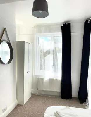 a bedroom with a window with black curtains and a mirror at Spacious 4-Bed Home Near Cambridge City Centre in Chesterton