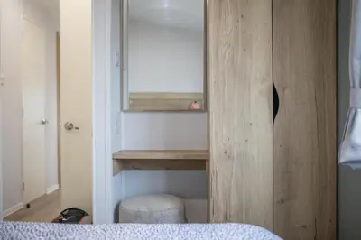 a bedroom with a mirror and a wooden cabinet at New - 3 bedroom Caravan, 140 Pasture Lane in Great Clacton