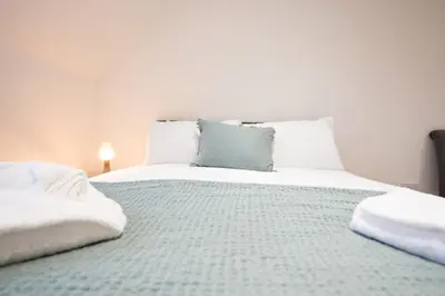 a bedroom with a large bed with white sheets and blue pillows at Stylish 2BR in Wickham Market in Wickham Market