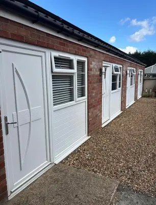 a row of white garage doors on a brick building at White hart public house in Ashill