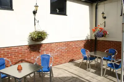 a patio with tables and chairs and a brick wall at Farmhouse Inn in Thaxted
