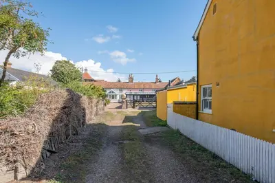 a dirt road next to a yellow building at 2 Beach Cottages, Thorpeness in Thorpeness