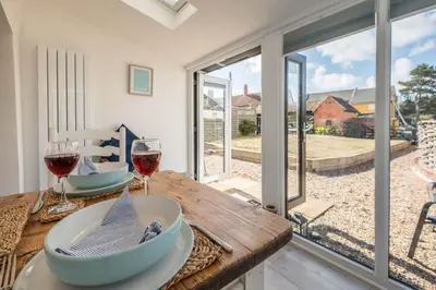 a table with two glasses of wine on it with a view of the patio at 2 Beach Cottages, Thorpeness in Thorpeness