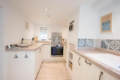 a kitchen with white cabinets and a wooden floor at 2 Beach Cottages, Thorpeness in Thorpeness
