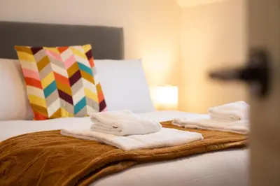 a bed with towels on it with a colorful pillow at 4 The Royal Serviced Apartments, Harwich - Garden- Parking-Fast WiFi in Parkeston