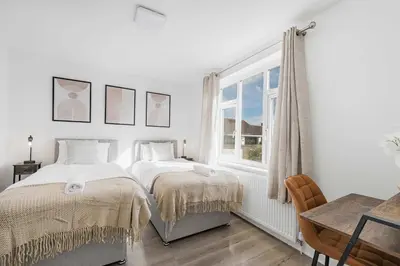 a white bedroom with two beds and a window at Modern Comfort 4BR House in Colchester