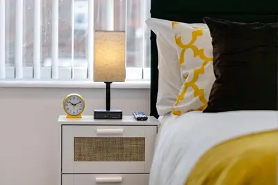 a bed with a lamp and a clock on a night stand at Cosy and Peaceful flat in Benfleet close to station in South Benfleet