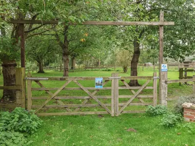 a wooden gate in a field with trees at Carabelle Cow Shed 7 in Woodbridge
