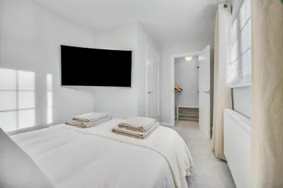 a white bedroom with a flat screen tv on the wall at Lovely 2-Bed House with parking in Broomfield