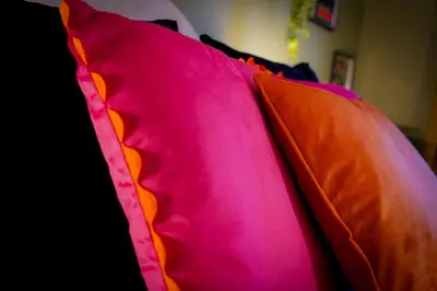 a pink and orange pillow sitting on a bed at Bright & Spacious 5-Bedroom Stay near Cambridge in Hardwick