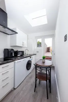 a kitchen with white cabinets and a table and a chair at Jayjay Guest House in Basildon