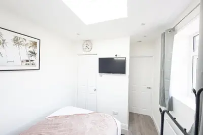 a white bedroom with a bed and a tv at Jayjay Guest House in Basildon