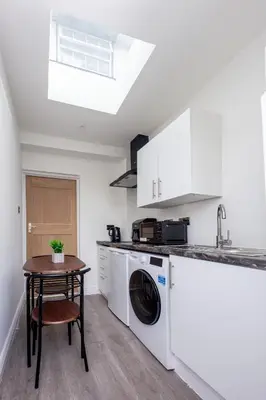 a kitchen with a washing machine and a table at Jayjay Guest House in Basildon