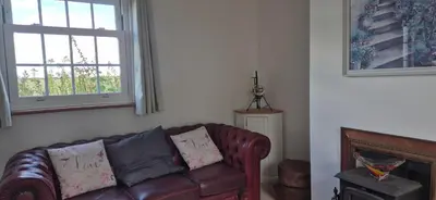 a living room with a leather couch and a window at Cambridgeshire Cosy Cottage in Cottenham