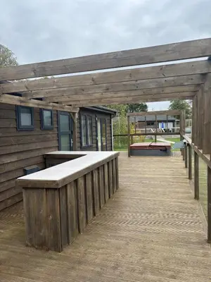 a wooden deck with a bar and a bench at Contemporary 3 bed luxury Spa lodge with hot tub in Bury Saint Edmunds