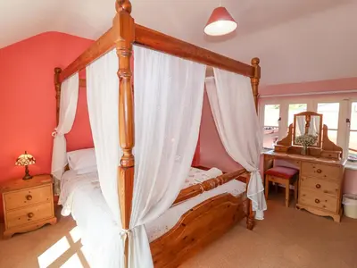 a bedroom with a wooden canopy bed with white curtains at Coachman's Cottage in Ipswich