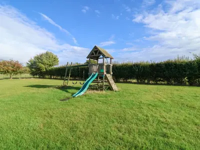 a playground with a slide in the middle of a field at Coachman's Cottage in Ipswich