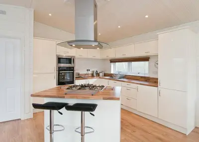 a kitchen with white cabinets and a island with bar stools at Warren Lodges in Little Baddow