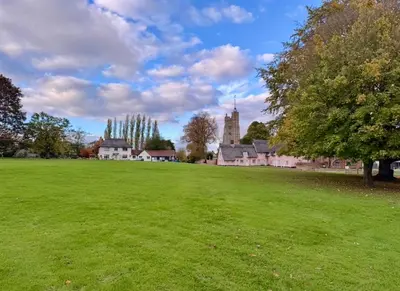 a large green field with a church in the background at Manor Cottage in Cavendish