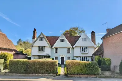 a white house with a fence and bushes at Manor Cottage in Cavendish