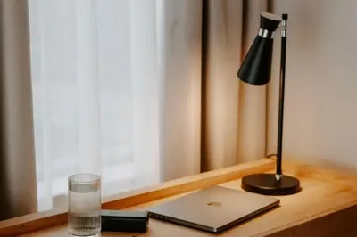 a desk with a laptop and a lamp and a glass at The Hobson Cambridge by Adina in Cambridge