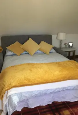 a bed with a yellow blanket and pillows on it at Sunnyside Cottage in Great Sampford