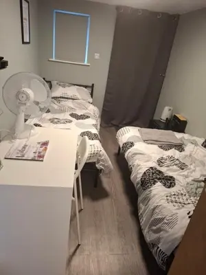 a room with two beds and a desk with a fan at Als air b and b in Cherry Hinton