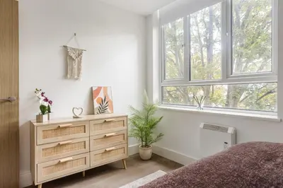 a bedroom with a bed and a dresser and two windows at Stonebridge House Apartment in Chelmsford