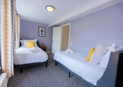 two beds in a room with blue walls and yellow pillows at Stylish central location 3 bedroom house in Ely