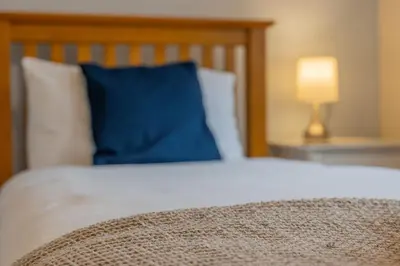 a bed with a blue pillow and a lamp on a table at Top Step Cottage in Aldeburgh